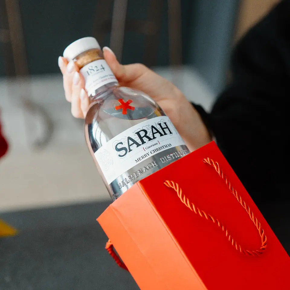 A personalised Caorunn gin bottle lifted out of a red gift bag