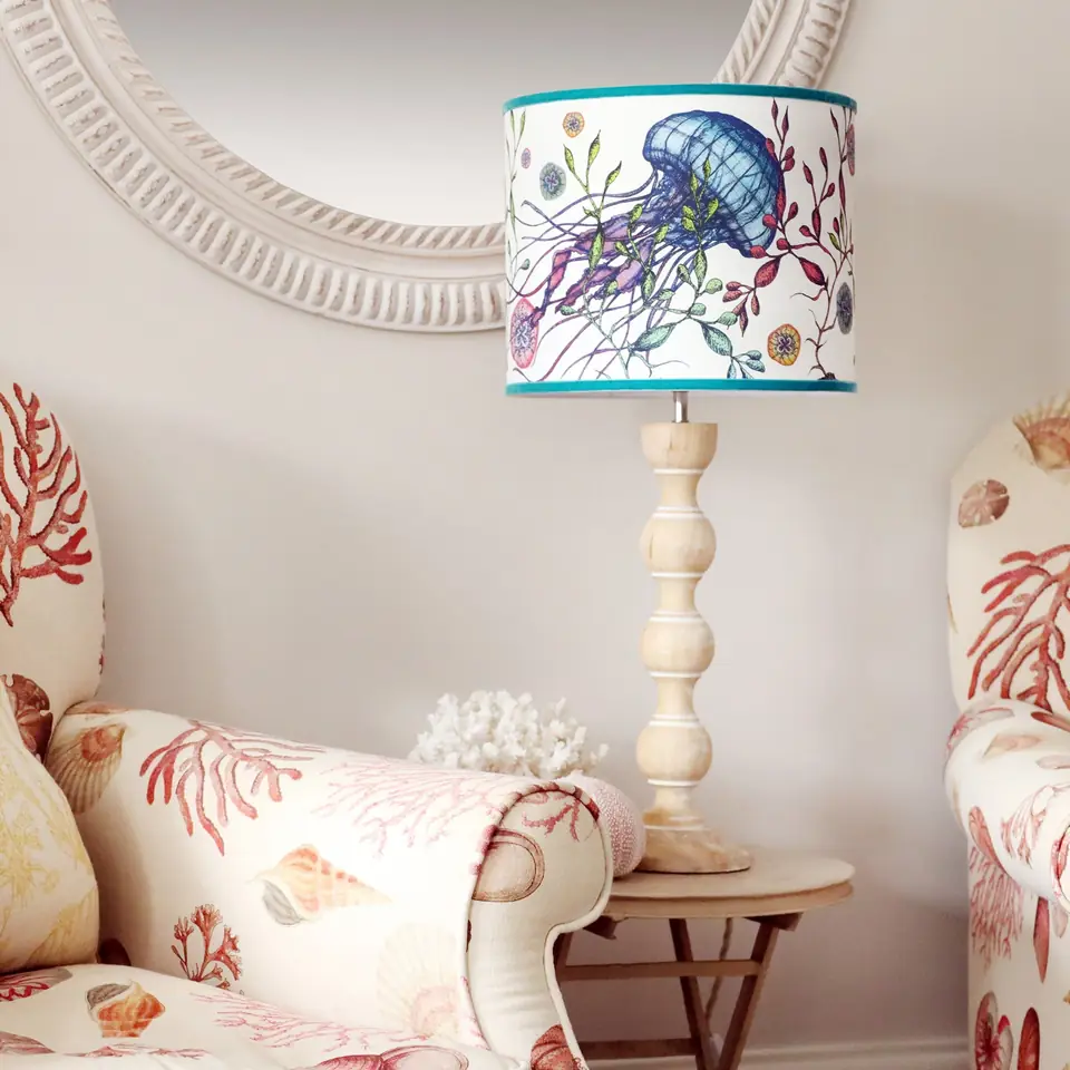 A jellyfish-print lampshade on a whitewashed bobbin lamp base, beside a coral-print chair