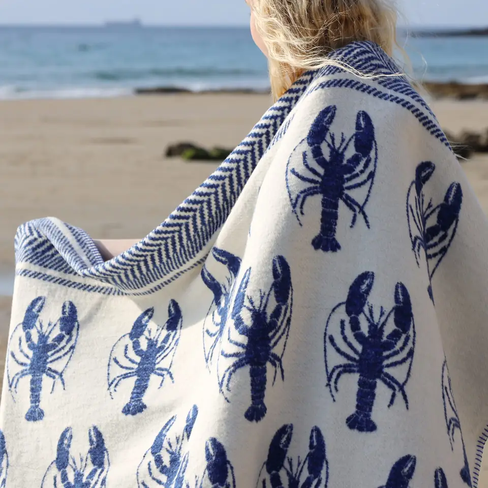 A cobalt blue and ecru lobster-print throw draped over a shoulder on a beach