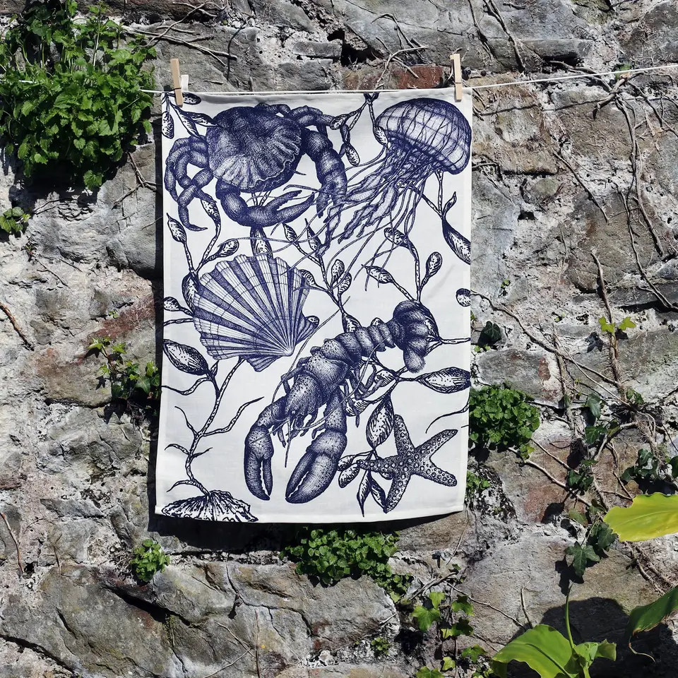 A navy sea-creature print tea towel pegged out against a stone wall