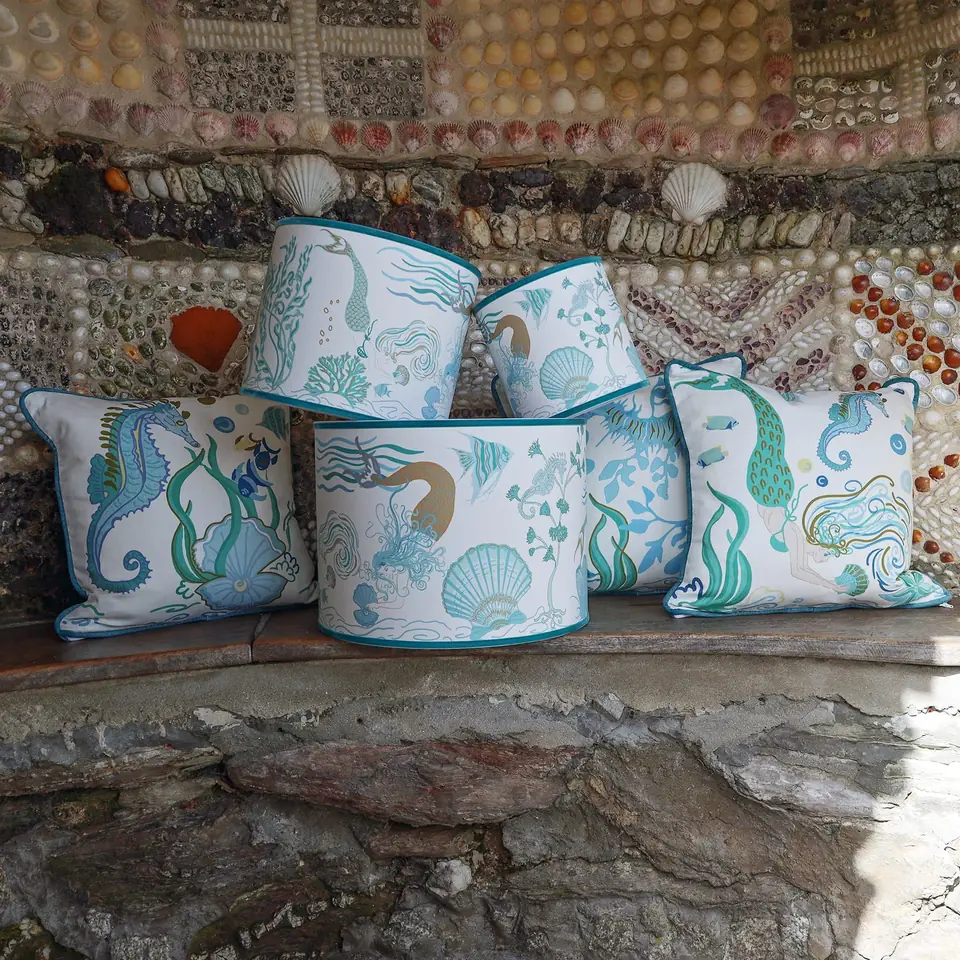 Turquoise seahorse and shell-print cushions and lampshades stacked against a shell-covered wall