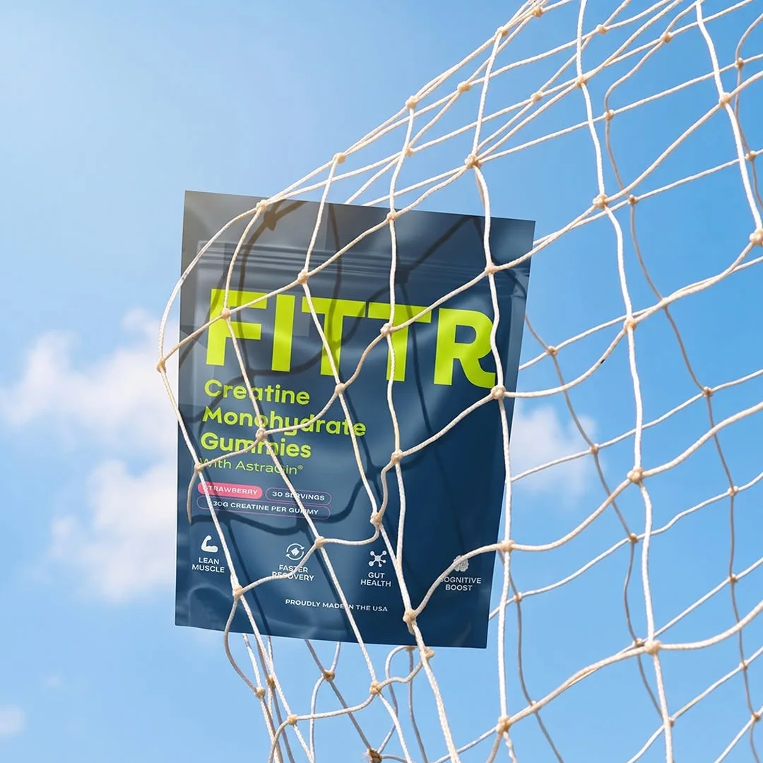 A pack of Fittr creatine gummies hanging in a net against a blue sky