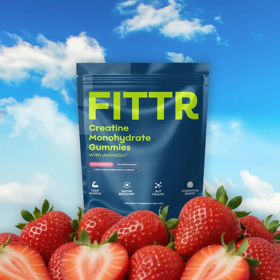 A pouch of Fittr creatine gummies rising out of fresh strawberries under a blue sky
