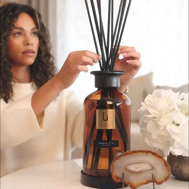 A woman arranging reeds in a large amber diffuser