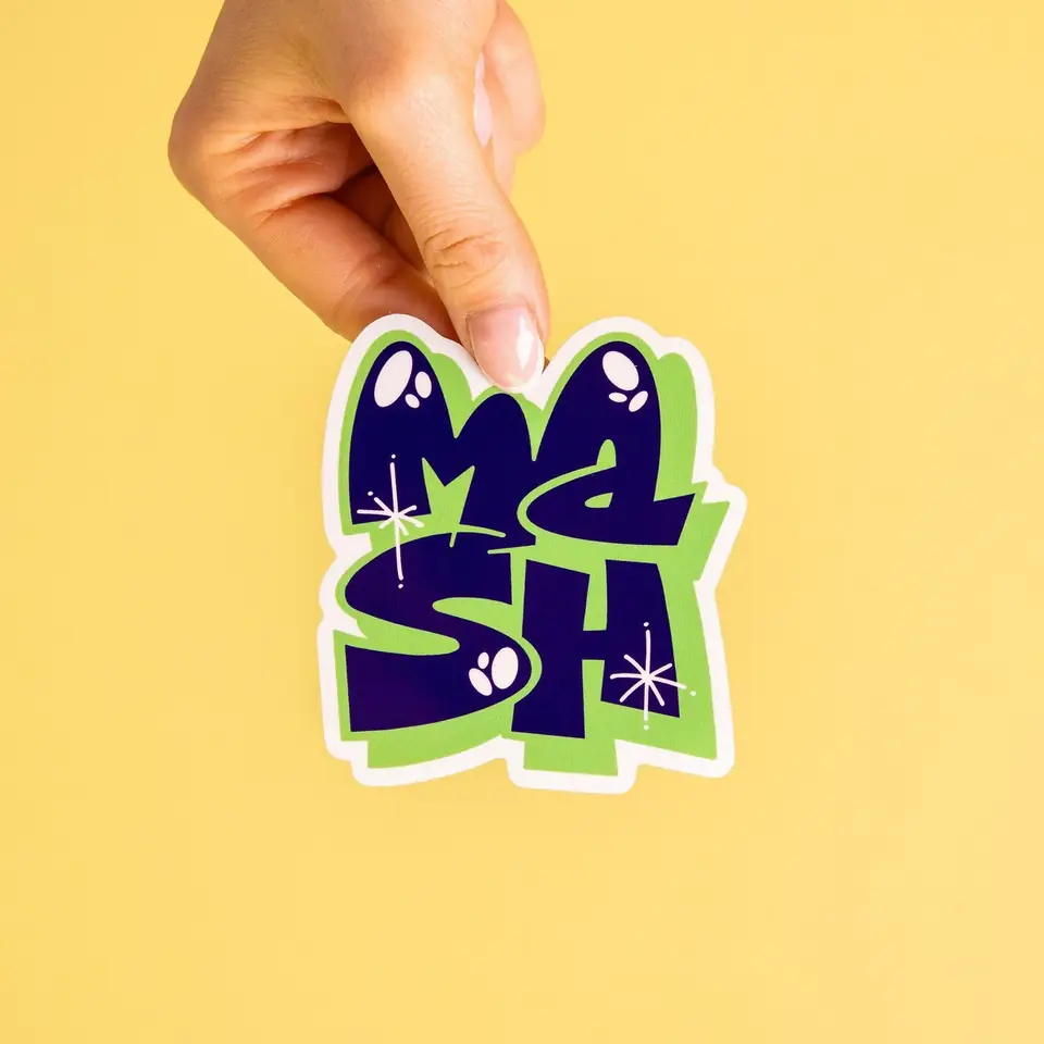 A hand holding a Mash lettering sticker against yellow
