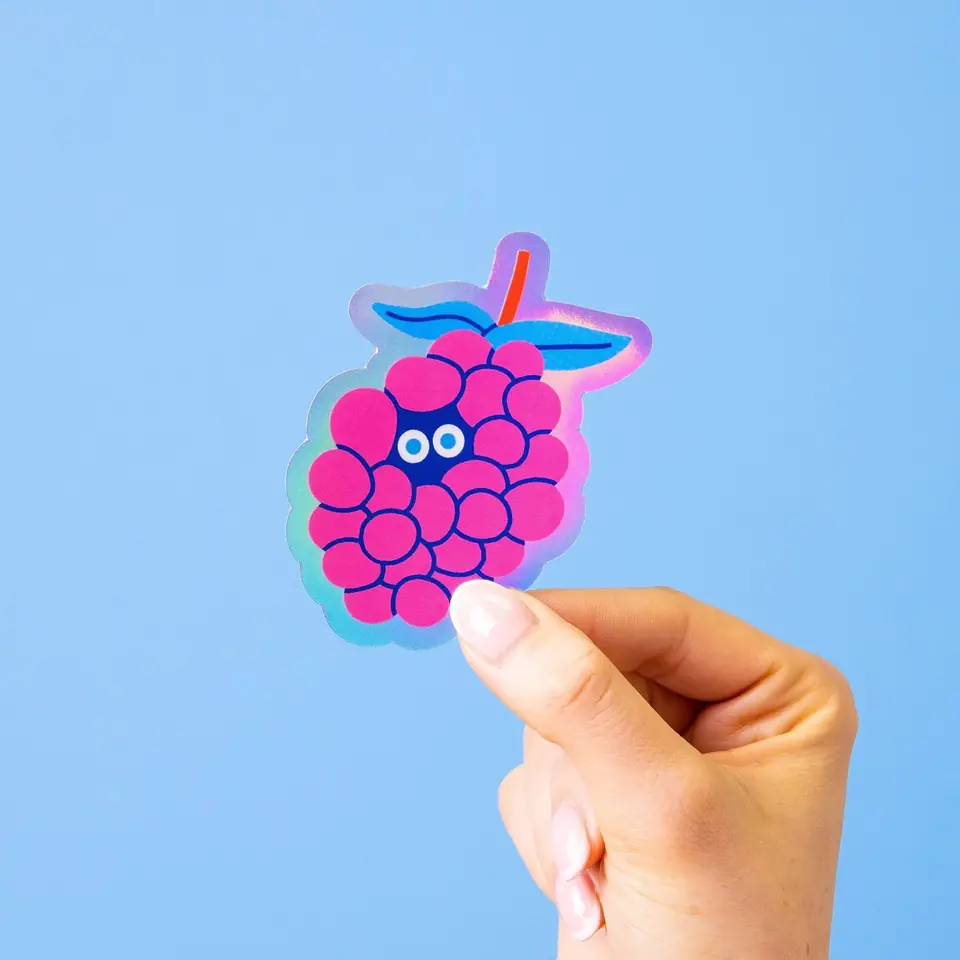 A hand holding a raspberry sticker against blue