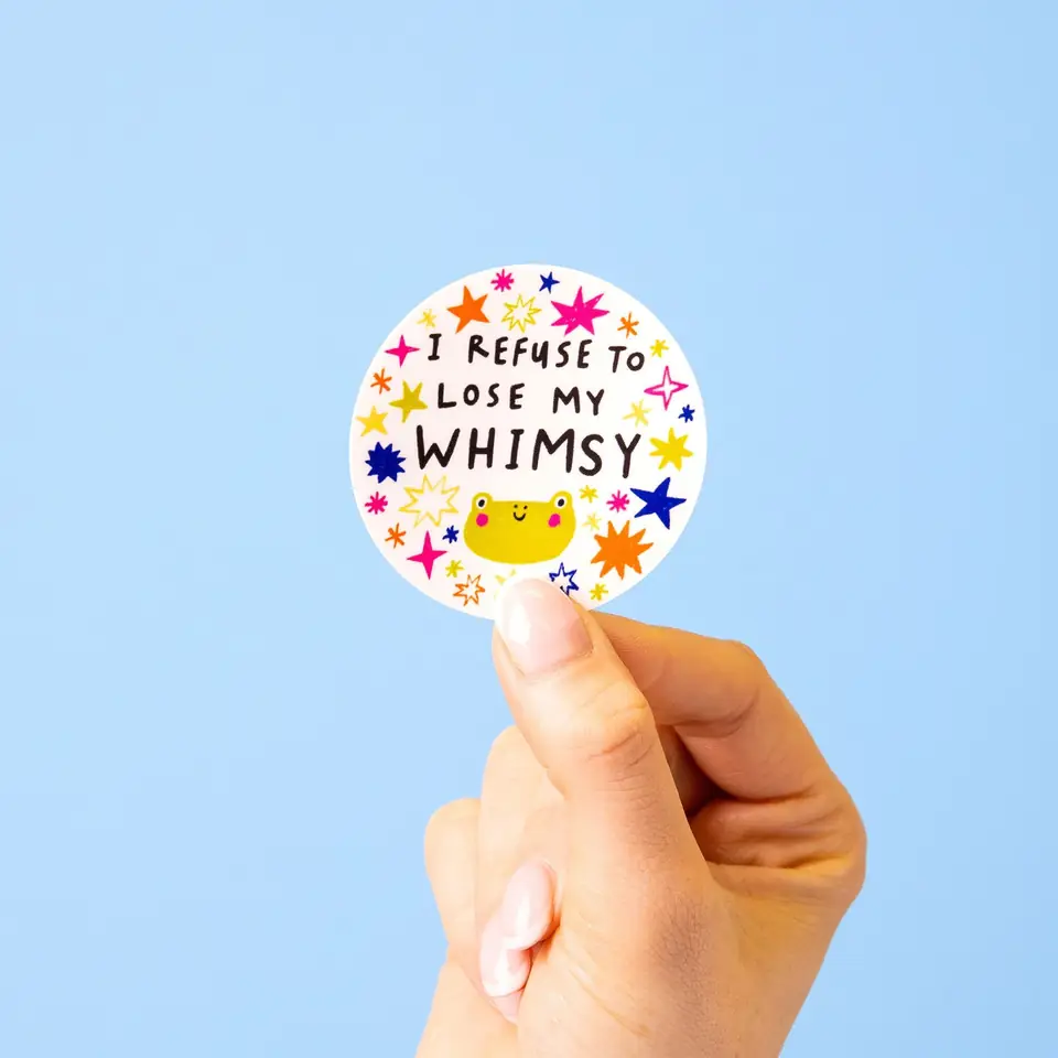 A hand holding a round whimsy sticker against pale blue