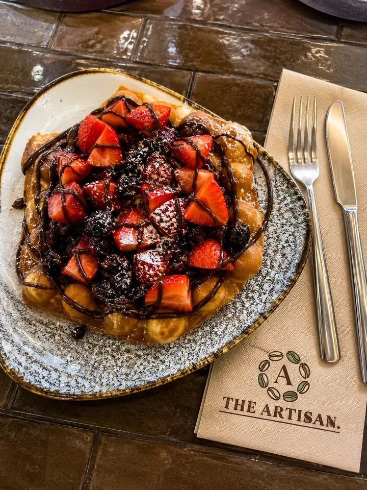 A waffle topped with strawberries and chocolate at The Artisan Coffee House