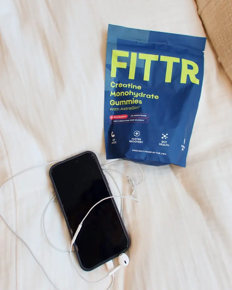 A pouch of Fittr creatine gummies on white bedsheets beside a phone
