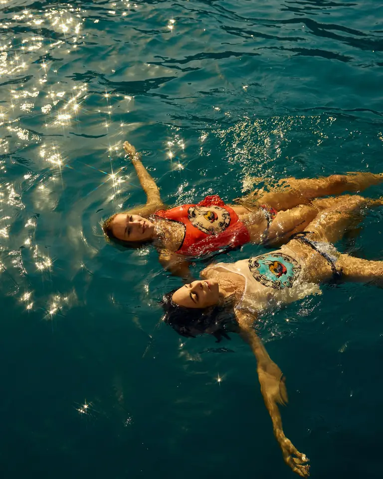 Two women floating in a pool wearing printed silk