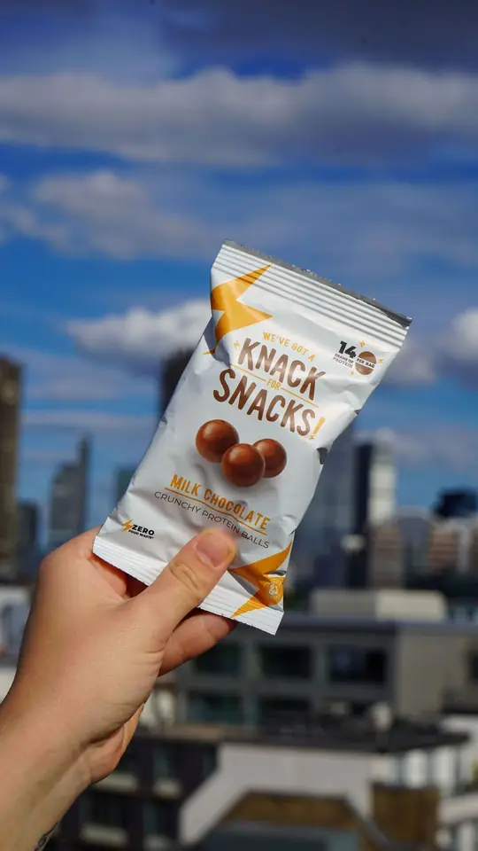 A hand holding a pack of Knack Snacks up against a city skyline