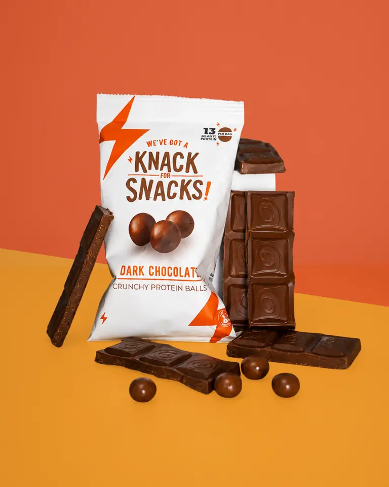 A pack of Knack Snacks dark chocolate protein balls beside broken chocolate on orange