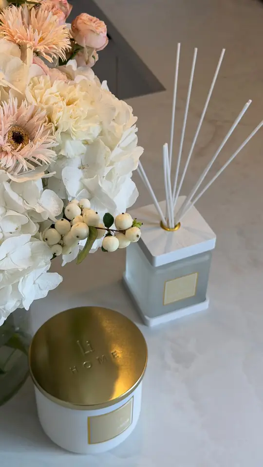 A reed diffuser beside white flowers on a marble surface