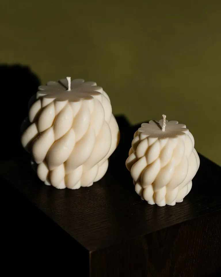 Two ivory braided pillar candles on a dark table against an olive wall