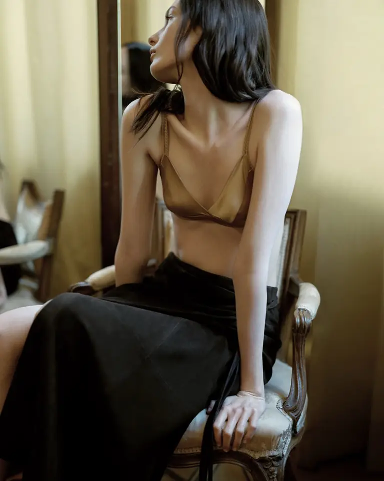 A model in a gold silk camisole seated on a cafe chair