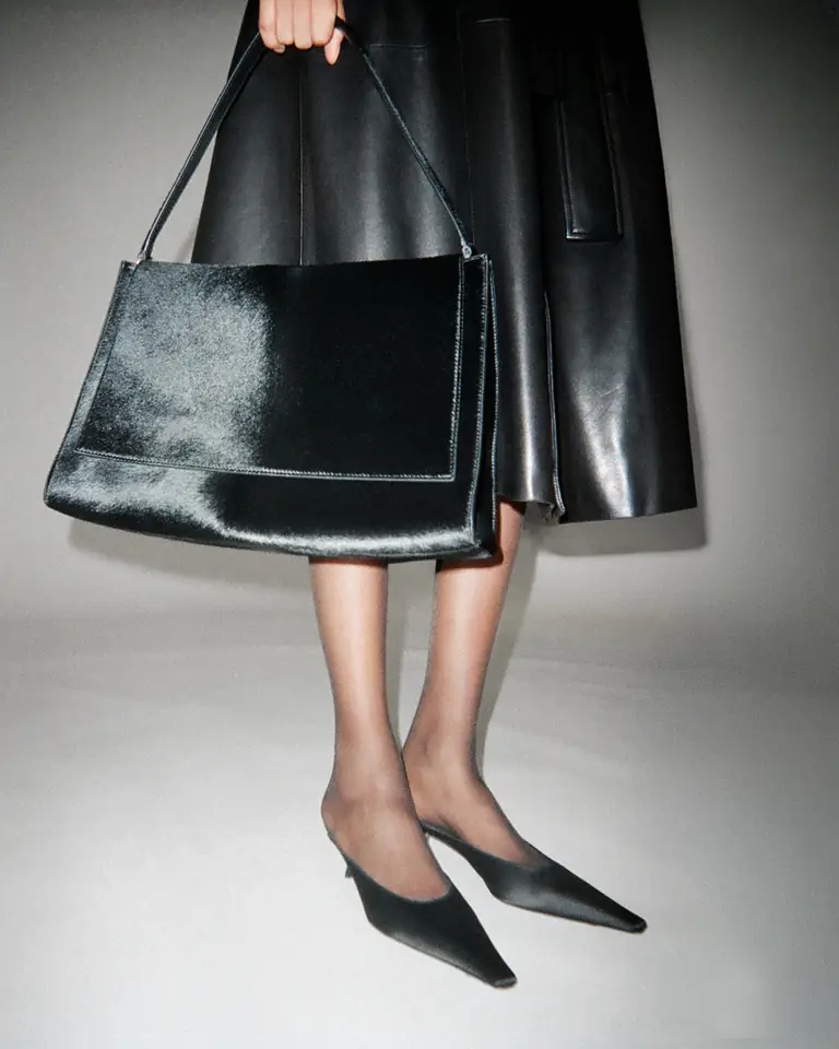 A black patent leather bag and pointed slingbacks below a long leather skirt