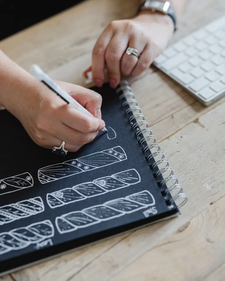 A hand sketching engagement ring designs in a notebook