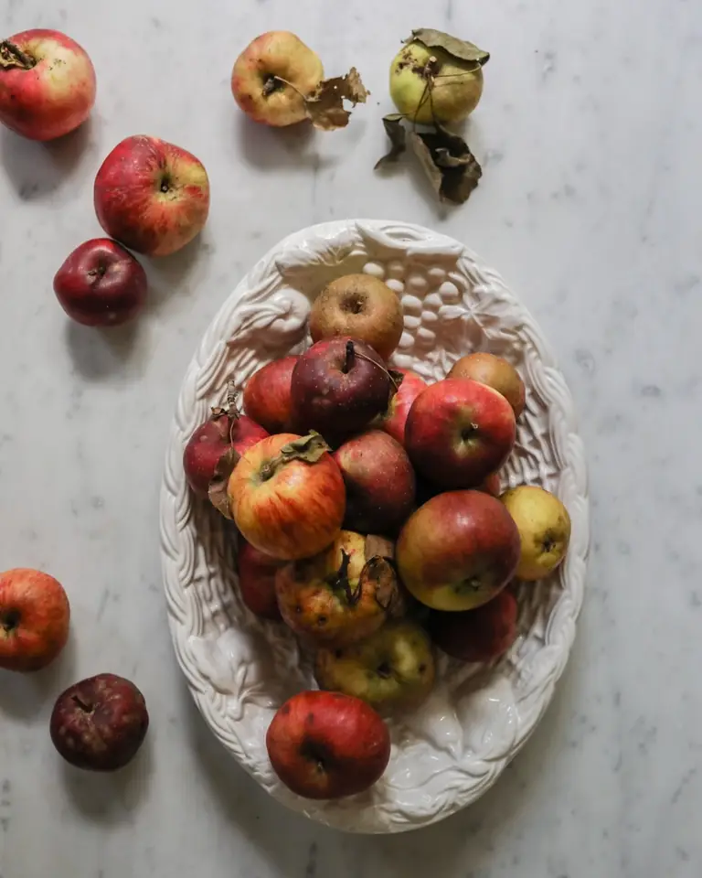 A white bowl of apples on a marble surface