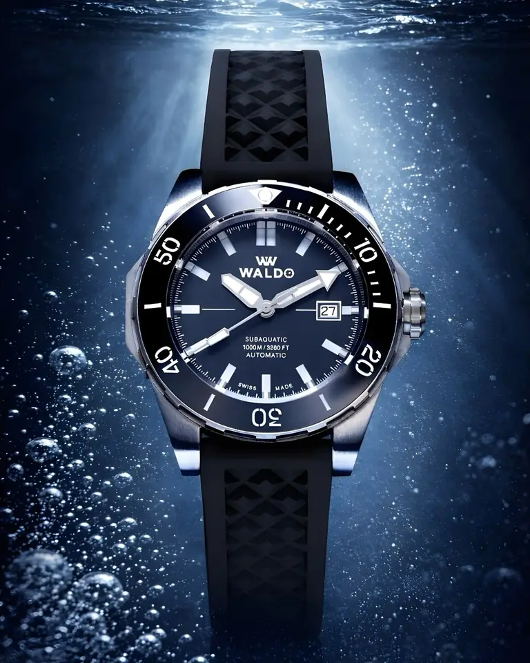 A Waldo dive watch on a black rubber strap, lit from above under water
