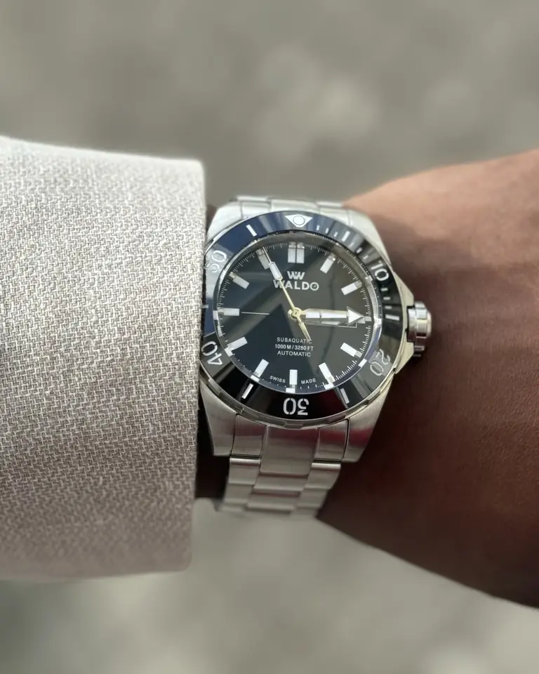 A Waldo watch with a blue dial on a wrist in a linen sleeve