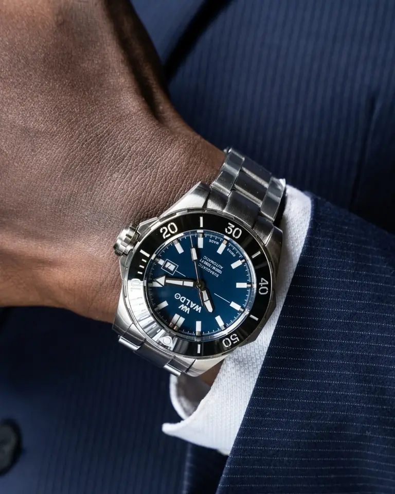 A Waldo watch on a wrist in a navy suit sleeve