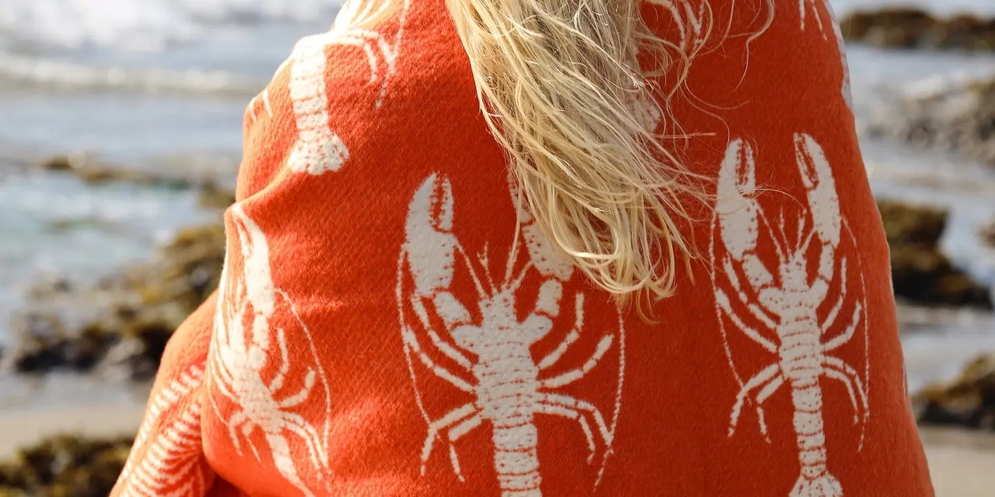 A Cream Cornwall lobster-print throw worn on a Cornish beach