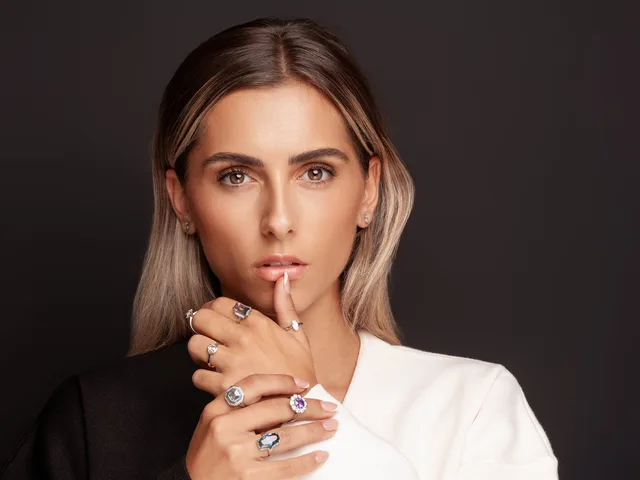 A model wearing several Poppy Elder rings, shot against black