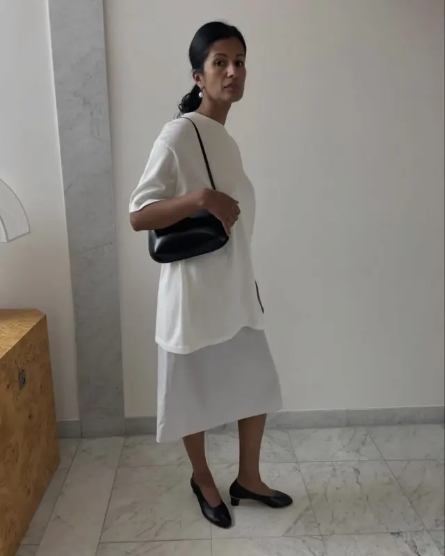 A Bessette look: an oversized white tee, a white midi skirt and a black shoulder bag