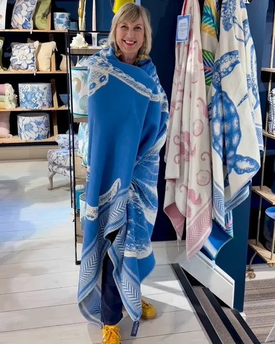 Inside a Cream Cornwall shop, wrapped in their blue octopus throw among coastal lampshades and cushions