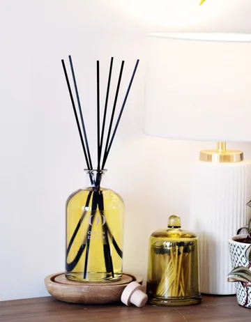 An Owen Drew reed diffuser and candle beside a lamp