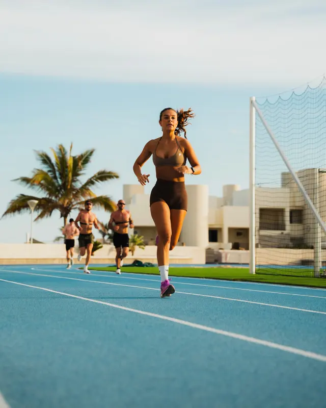 A Powerlete athlete running on an outdoor track in a matching bra and shorts